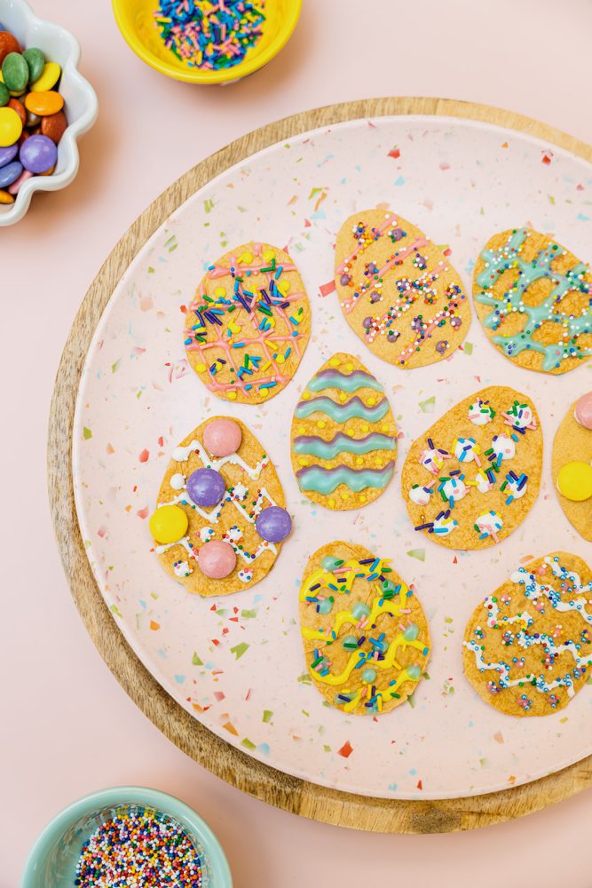 Chips de Pâques à base de tortillas Mejicano en forme d'œufs, décorées de crémage, de chocolat et de bonbons confettis colorés, servies sur une assiette.