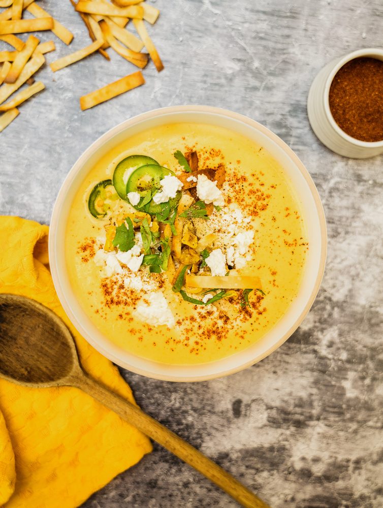 Chowder mexicaine avec chou-fleur, chili, maïs et jalapeno, garni de morceaux de tortillas croustillantes Mejicano, servi dans un bol avec une cuillère en bois et une serviette jaune.