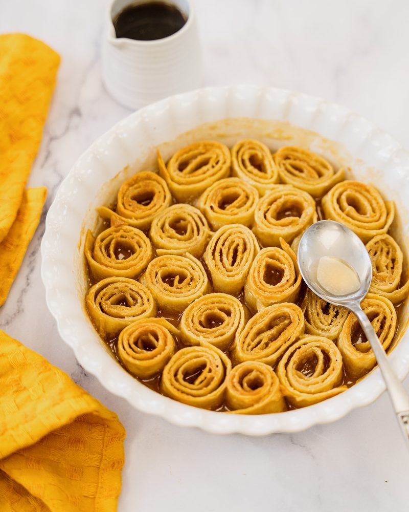 Mejicano tortillas-based sweet cinnamon rolls with brown sugar and butter, served in a dish, with a spoon, yellow napkin, and syrup.